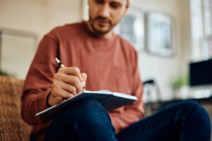 Close up of man writing in notebook at home.